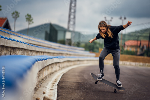 Teenage girl performing skateboard tricks on the sports field.