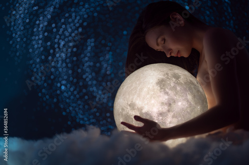 Naked girl with the moon in her hands on a background of stars, femininity and beauty female, clouds, magic and beauty photo