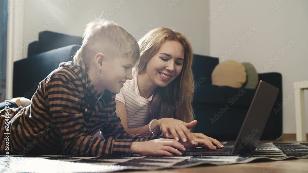 Concept of social networks. Portrait of teenage blond boy and his beautiful mother surfing the net and making new posts in internet social media profile. Spending time with family at home.