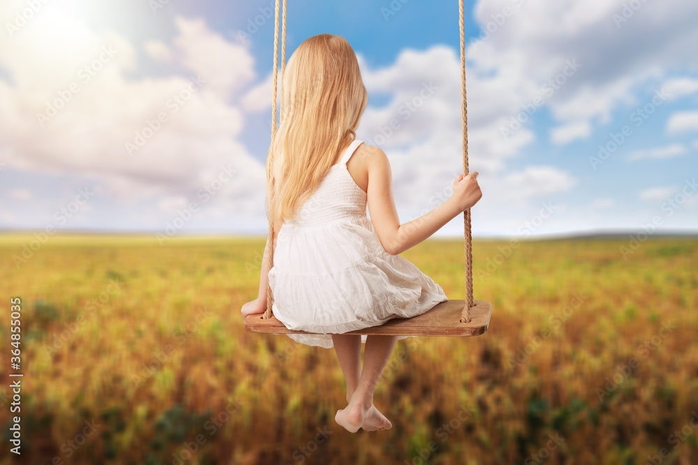 Little child blond girl having fun on a swing