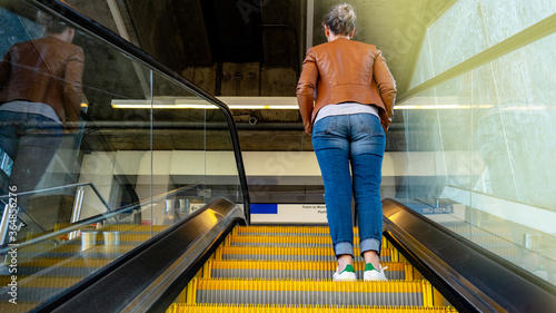 Young woman on the escalator on her way to the train station. Rear view of a woman climbing the escalator.