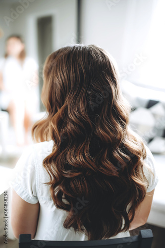 Healthy hair. Brunette woman with curly long hairstyle at the beauty salon. Back view of hairs. Hair salon styling concept.