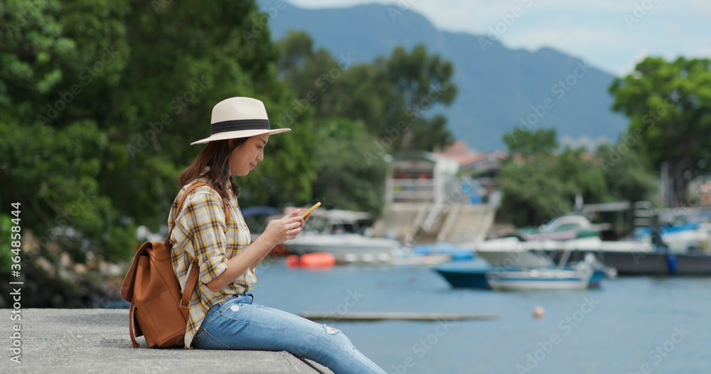 Woman looks at the cellphone and sits on pier