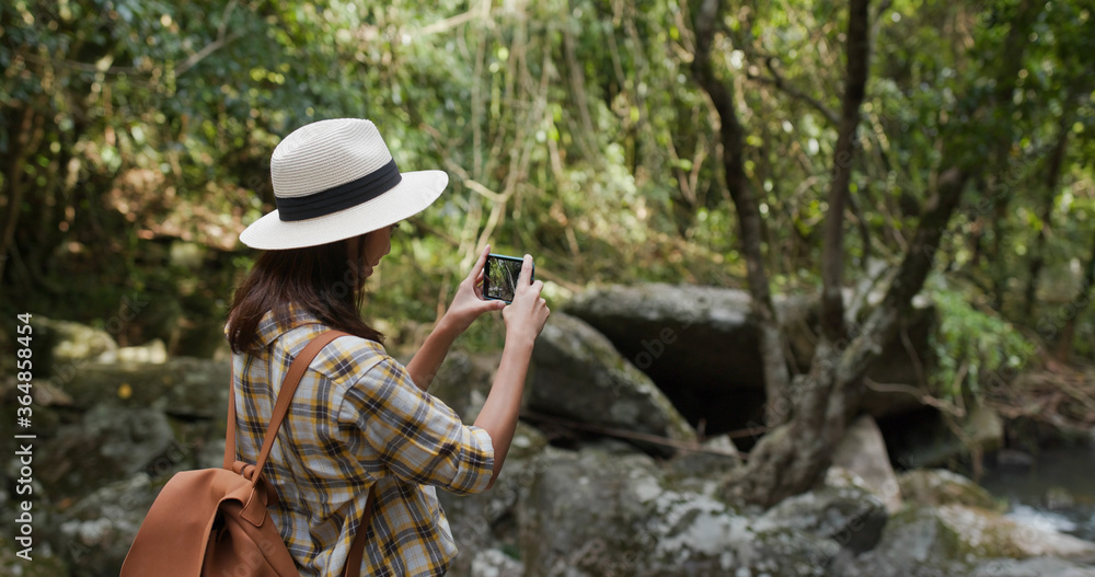 Woman goes hiking, use cellphone for take photo in forest