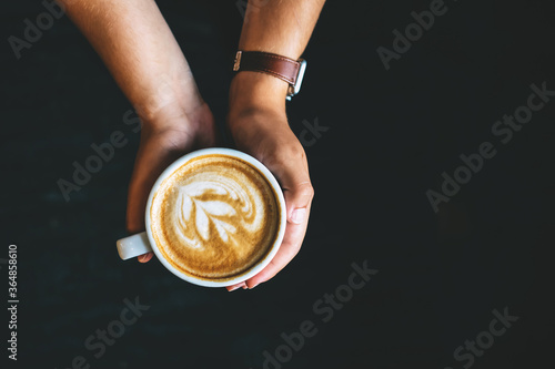 Male hands holding cup of hot latte on dark background. Take a break concept