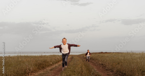 A little boy in jeans clothes runs, arms outstretched towards the viewer across the field. The sky is cloudy. Image with a selective focus