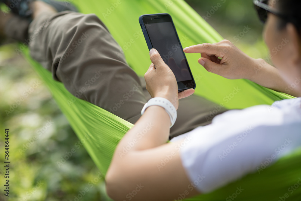 Relaxing in hammock hand using smartphone in tropical forest