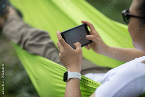 Relaxing in hammock hand using smartphone in tropical forest