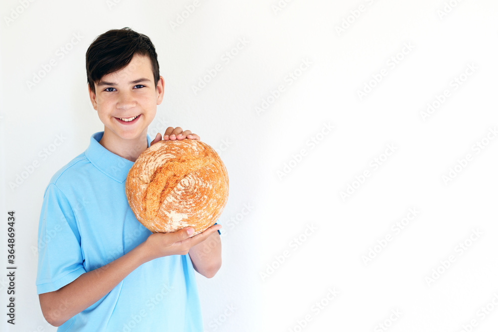 A teenager boy holds rustic homemade fresh bread in his hands. Light background, daylight, indoor. Copy space A teenager boy holds rustic homemade fresh bread in his hands. Light background, daylight, indoor. Copy space