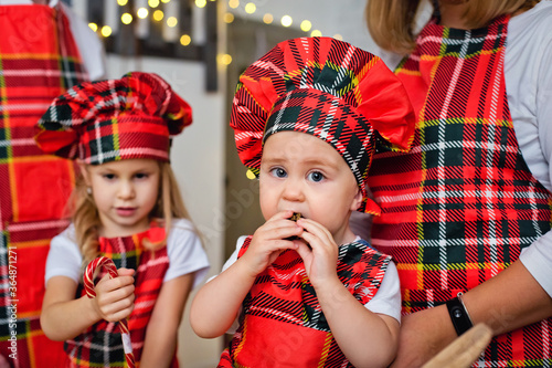 A child in a chef's hat and apron prepares cookie dough for Christmas. Children prepare sweets in the kitchen with a Christmas tree on a snowy winter day.