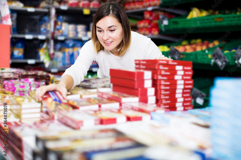 Fototapeta premium Beautiful young woman choosing delicious sweets in supermarket