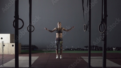 Young adult sporty woman performing skipping rope workout in cross fit gym