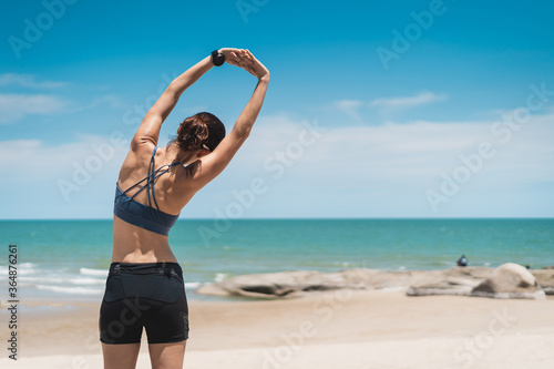 Young Asian sporty woman wearing sports wear and stretching on the beach. Female working out outdoor in summer season