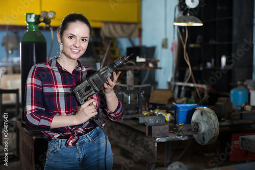 Portrait of young female master standing with drill in workshop