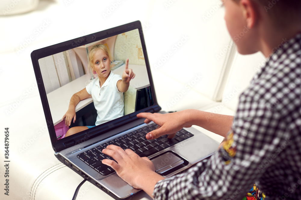 The boy communicates using a webcam on a laptop while sitting at home . Friends communicate via video conferencing The boy communicates using a webcam on a laptop while sitting at home . Friends communicate via video conferencing