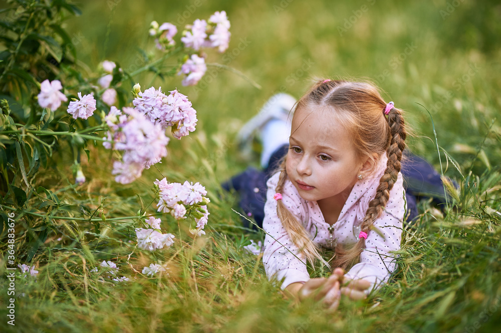 The little girl lies on the grass and holds her head with her hands. Girl makes different facial expressions The little girl lies on the grass and holds her head with her hands. Girl makes different facial expressions
