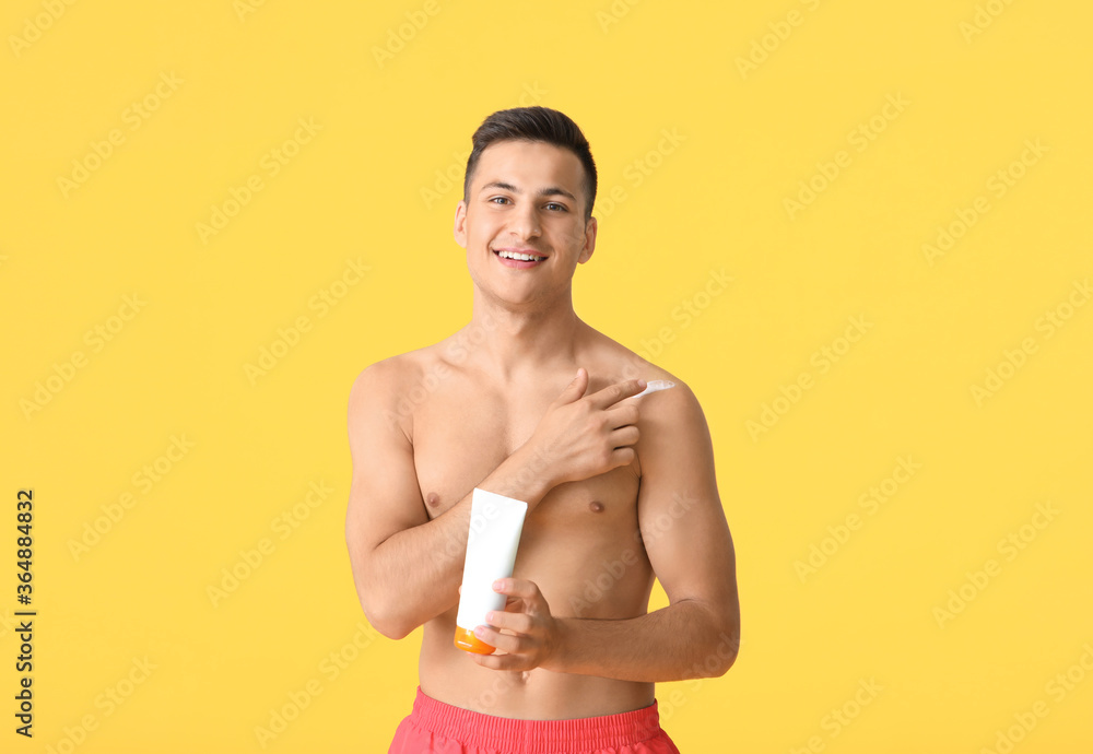 Happy young man with sun protection cream on color background