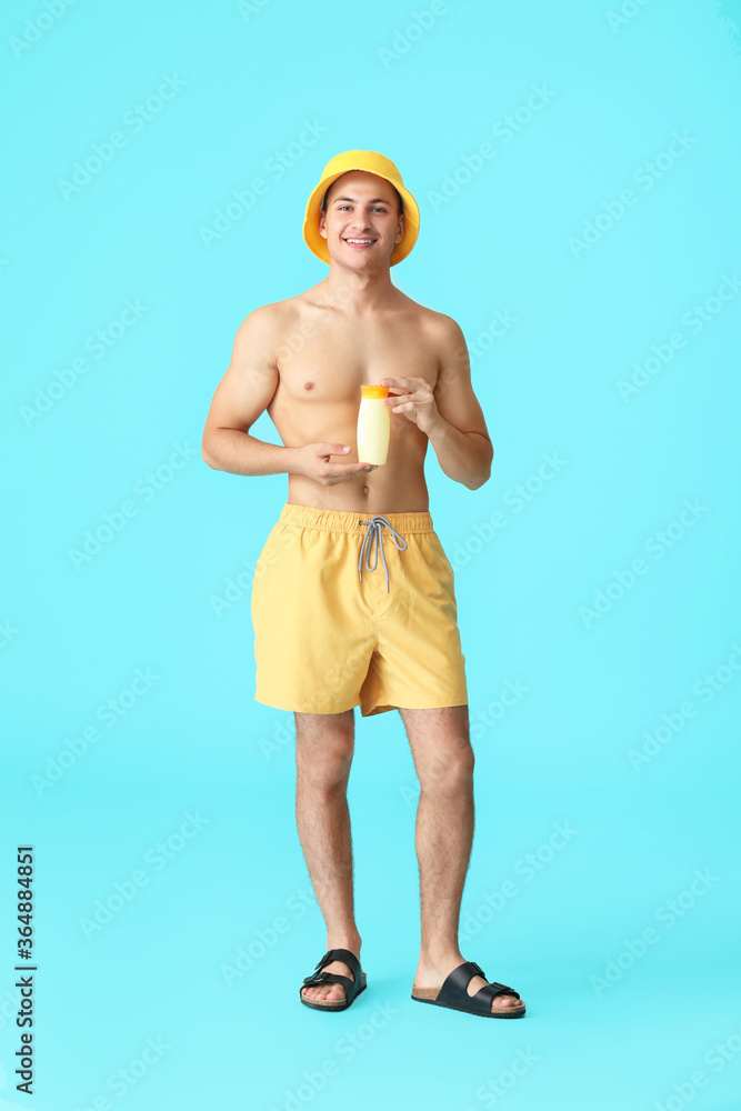 Happy young man with sun protection cream on color background