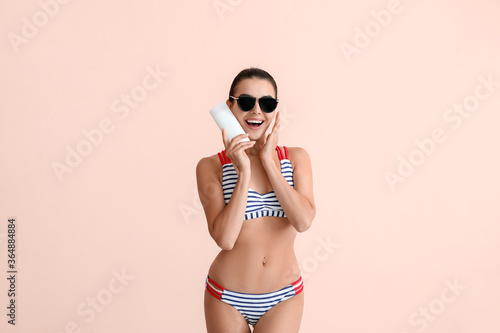 Happy young woman with sun protection cream on color background © Pixel-Shot