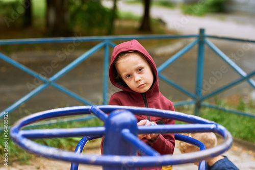 Little girl alone rides a carousel in the playground and she is very sad. all her friends are in quarantine. COVID-19