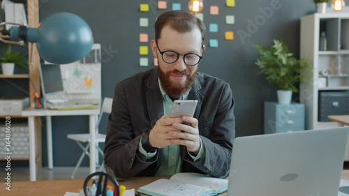 Handsome businessman is using smartphone in office at desk enjoying communication online touching screen. Modern technoology and businesspeople concept. photo