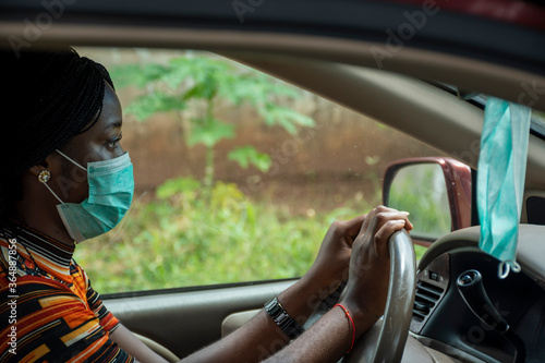young african woman driving and wearing a face mask