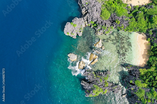 Matukad Island, Caramoan Islands, Philippines. Wild white sand beach. Summer and travel vacation concept. Rocky island with a white sandy beach, top view. Aerial top view of ocean waves, beach and