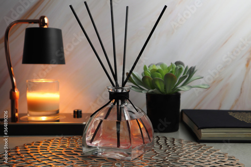 luxury aromatic reed diffuser glass bottle and candle warmer and book and small plant display on the grey table with background of marble wall in the bedroom
