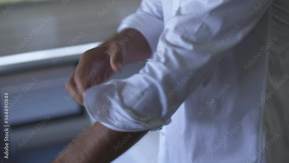 Man rolls up sleeves on his white dress shirt in his hotel room. Close up of arms / hands. Man rolls up sleeves on his white dress shirt in his hotel room. Close up of arms / hands.