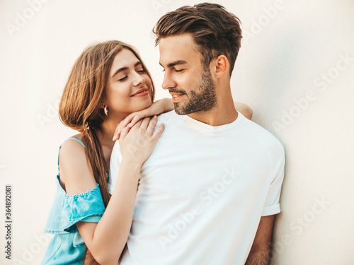 Portrait of smiling beautiful girl and her handsome boyfriend.Woman in casual summer jeans dress.Happy cheerful family.Female having fun.Couple posing in the street near white wall