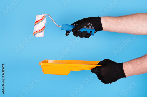 Hand in working glove with paint roller and plastic tray. Isolated on blue background.