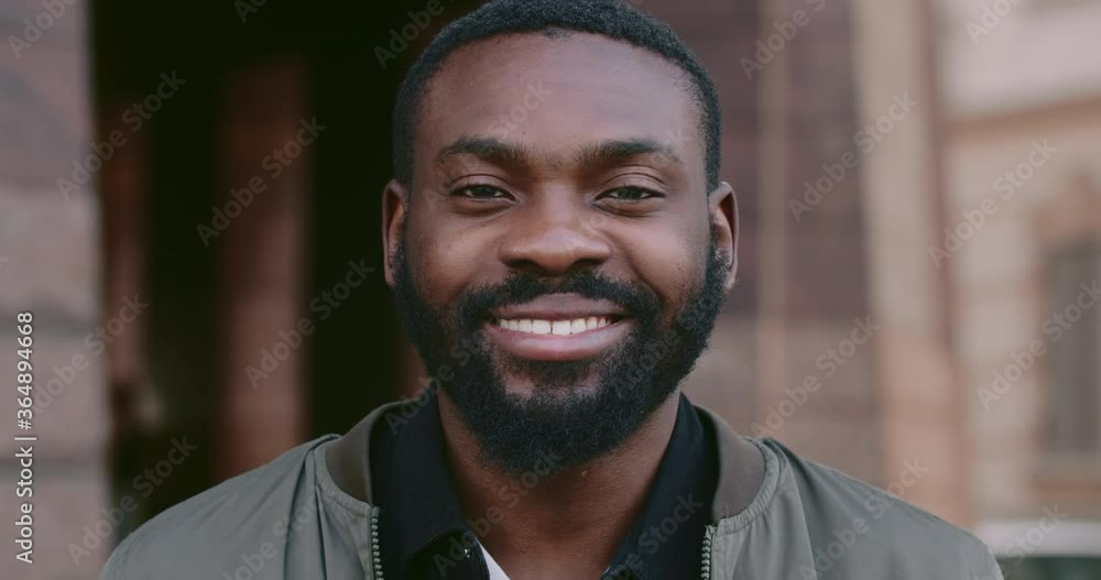 Facial portrait of young afro american man smiling while looking to camera. Close up of handsome bearded man with happy facial expression. Concept of emotions. Blurred background Facial portrait of young afro american man smiling while looking to camera. Close up of handsome bearded man with happy facial expression. Concept of emotions. Blurred background