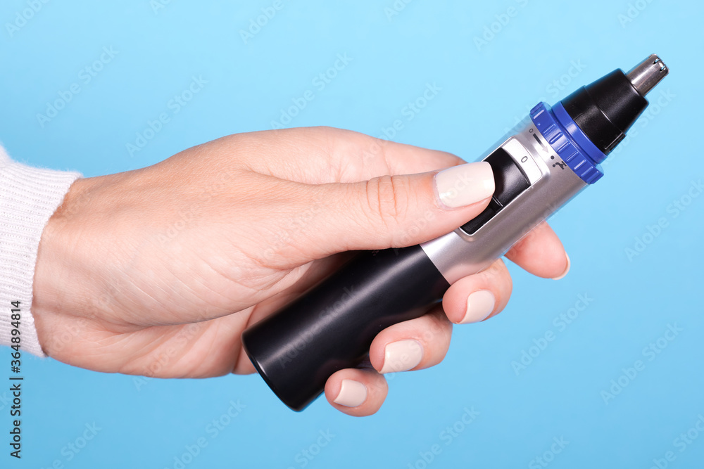 Hand with nose trimmer, hair electric cutter. Isolated on blue background. Hand with nose trimmer, hair electric cutter. Isolated on blue background.