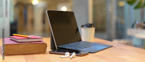 Study table with books, tablet with keyboard, smartphone, earphone and paper cup