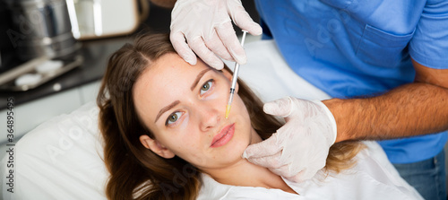 Young female patient receiving injections for face skin tightening in cosmetology clinic .