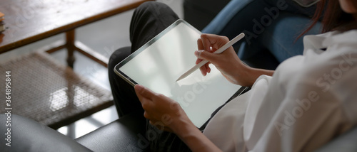 Fotografie, Tablou Female using mock up tablet with stylus while sitting on sofa in living room