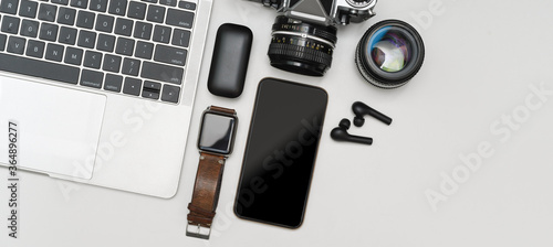 Digital devices on white table with laptop, smartphone, smartwatch, camera, earphone and copy space