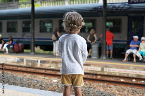 Beautiful curly-haired boy at the station looks at the train