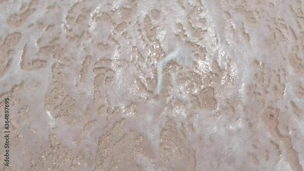 Close-up slow motion shot of sea waves breaking on sandy coastline. Top down view.