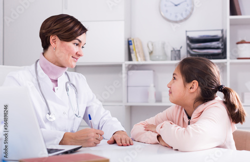 Doctor fills patient's card for girl and asks her about health in medical office © JackF