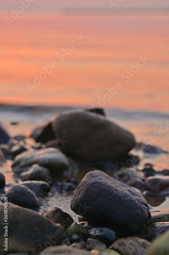 Sea sunset, pebbles on the seashore and a large stones in the foreground and against the background of the orange sea and the setting sun