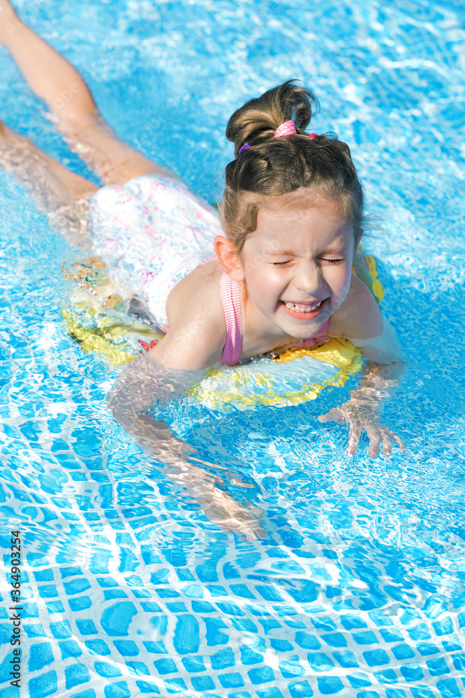 A funny little girl swims in a pool with clear blue water in a yellow lifebuoy in Sunny weather. The concept of rest, travel. A funny little girl swims in a pool with clear blue water in a yellow lifebuoy in Sunny weather. The concept of rest, travel.