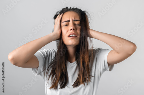 Oh NO! Photo of beautiful girl with long chestnut hairs, with closes eyes, astonished holding hands on head. Problems, surprise, fear, fobia concept