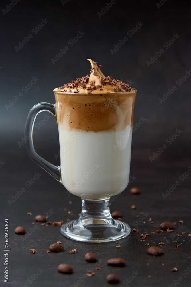 Glass of trendy fluffy creamy dalgona or whipped instant coffee with milk, coffee beans and chocolate on the dark background. New popular food and drink trend concept. Copy space. Glass of trendy fluffy creamy dalgona or whipped instant coffee with milk, coffee beans and chocolate on the dark background. New popular food and drink trend concept. Copy space.