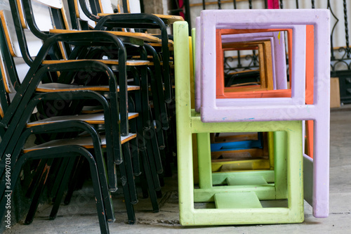 Conjunto de sillas de metal verde y madera apiladas junto con otra pila de sillas de madera de colores con formas cuadradas