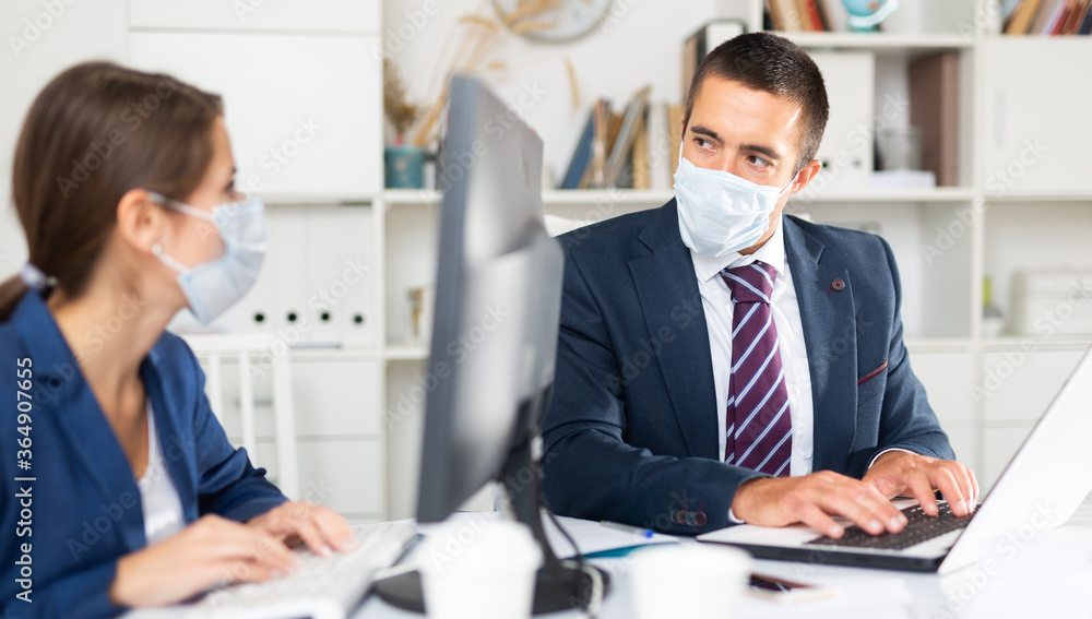 Fototapeta premium Portrait of businessman wearing protective face mask working in office with female colleague. Pandemic precautionary concept