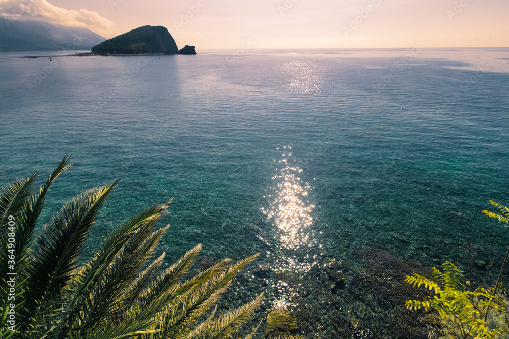 Sunlit path over Adriatic sea. Sun glare on the surface of the sea. Palm leaves on foreground