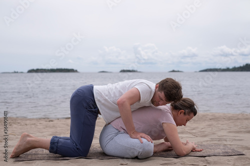 Man helping woman to do a yoga exercise butterfly pose or Baddha Konasana outdoor.