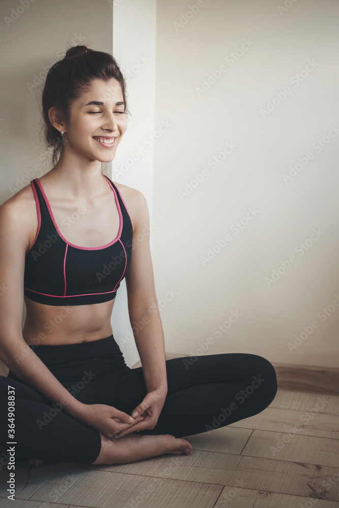 Smiling lady wearing sportswear is meditating on the floor at home near free space Smiling lady wearing sportswear is meditating on the floor at home near free space