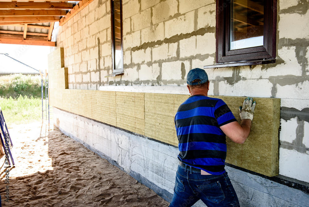 Worker insulates the house with mineral wool slabs. Internal thermal insulation of walls with mineral wool. Worker insulates the house with mineral wool slabs. Internal thermal insulation of walls with mineral wool.